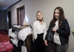 Dwie uczennice stoją przy wózku pracownika housekeepingu w korytarzu hotelu